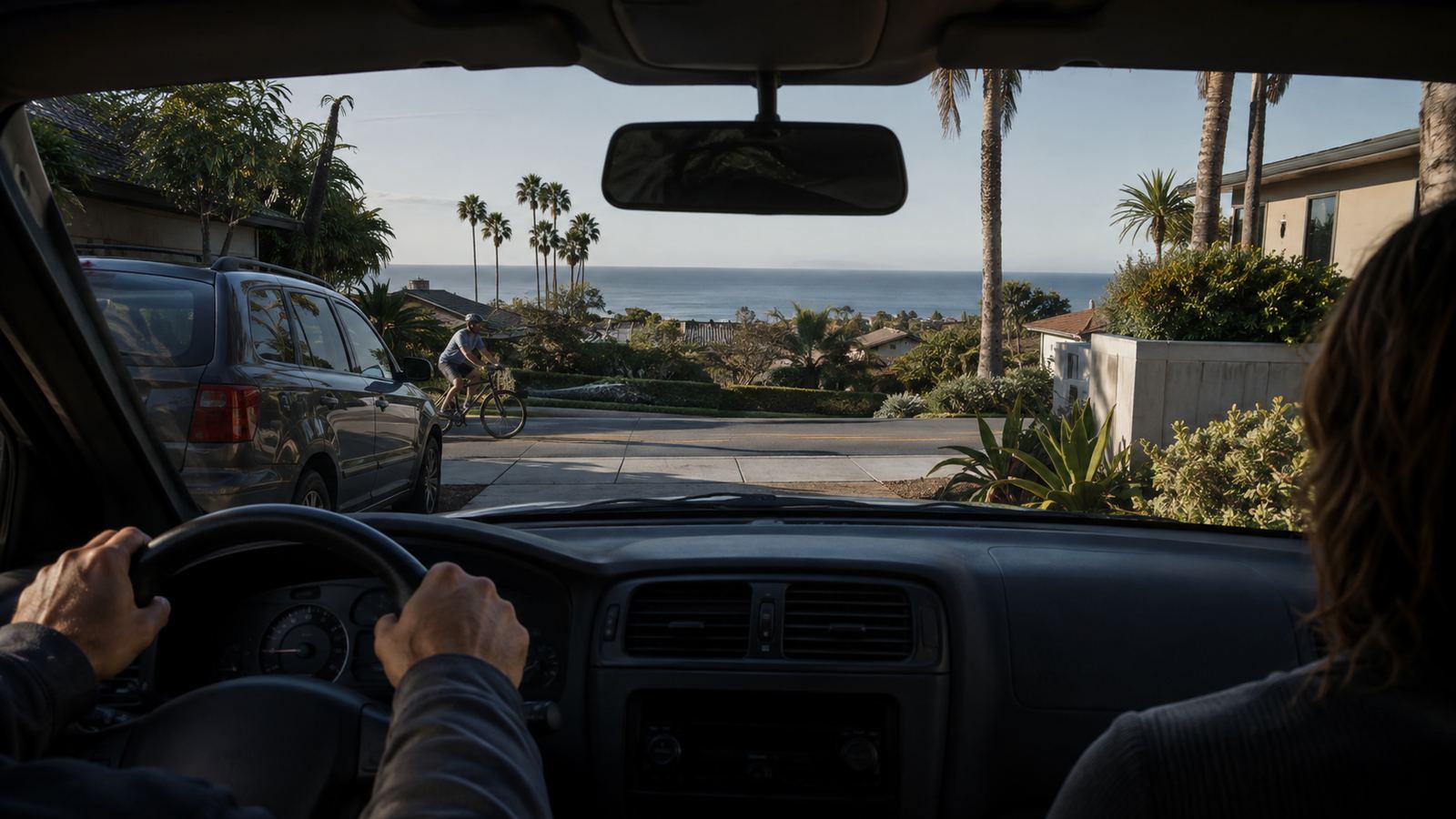 The view from the driver's seat backing out of a driveway, a parent in the passenger seat and a cyclist passing a parked SUV
